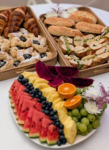 Hedelmä lautanen, täytettyjä patonkeja ja bageleita ja croisanntti.